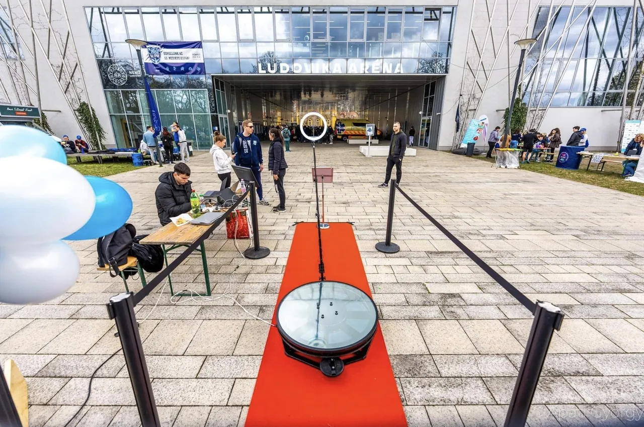 360°-os szelfigép platformja vörös szőnyeggel és kordonnal egy üvegtetős térben