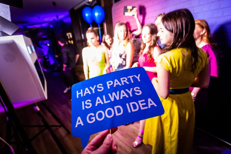 Céges parti vendégei neon fényben, előtérben a „Hays party is always a good idea” tábla