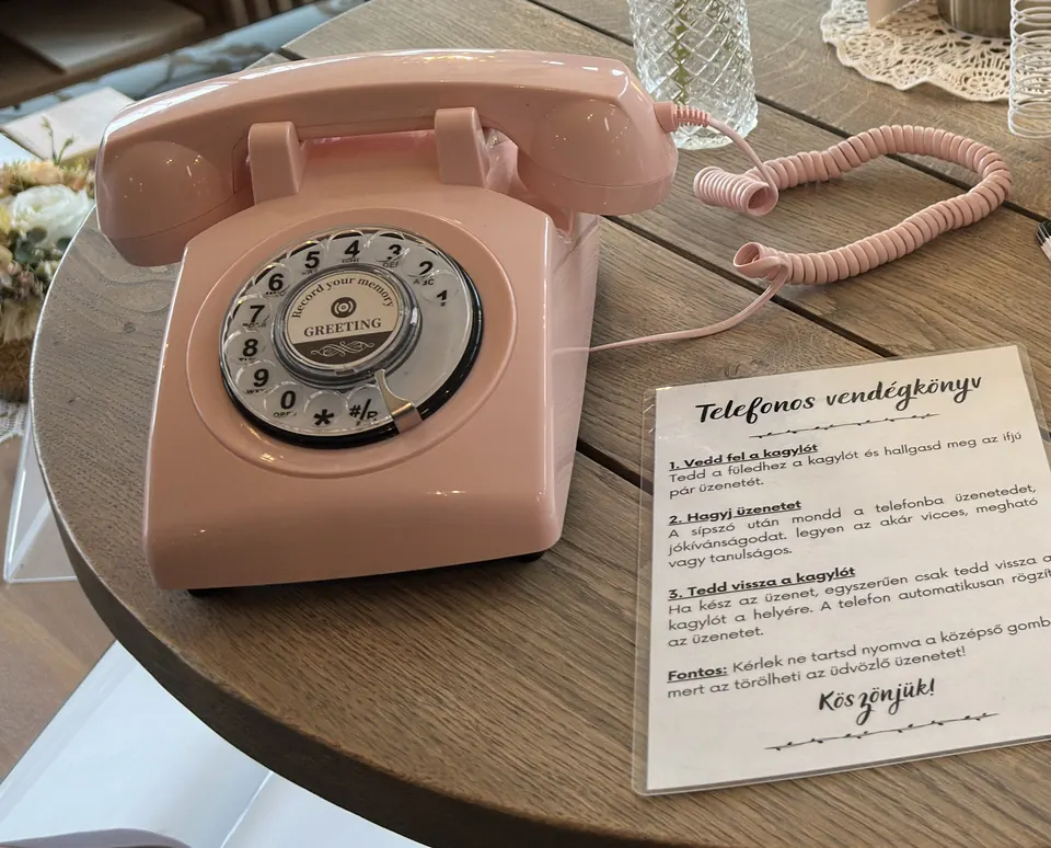 Rózsaszín retró telefon egy esküvői asztalon, mellette egy kártya